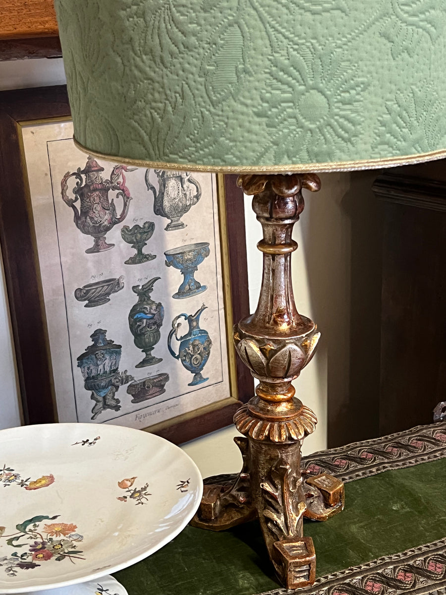 Lampada da tavolo con base in legno dorato scolpito adorato da decorazioni di ispirazione floreale e con paralume in tessuto verde decorato che aggiunge ulteriore eleganza al design complessivo.

Elegante pezzo d’arredamento dallo stile classico e sofisticato, un’aggiunta perfetta per coloro che cercano un tocco di classe e storia nel proprio arredamento.

Misure lampada 15x40 cm Altezza totale 63 cm Paralume 30x29 cm&nbsp;