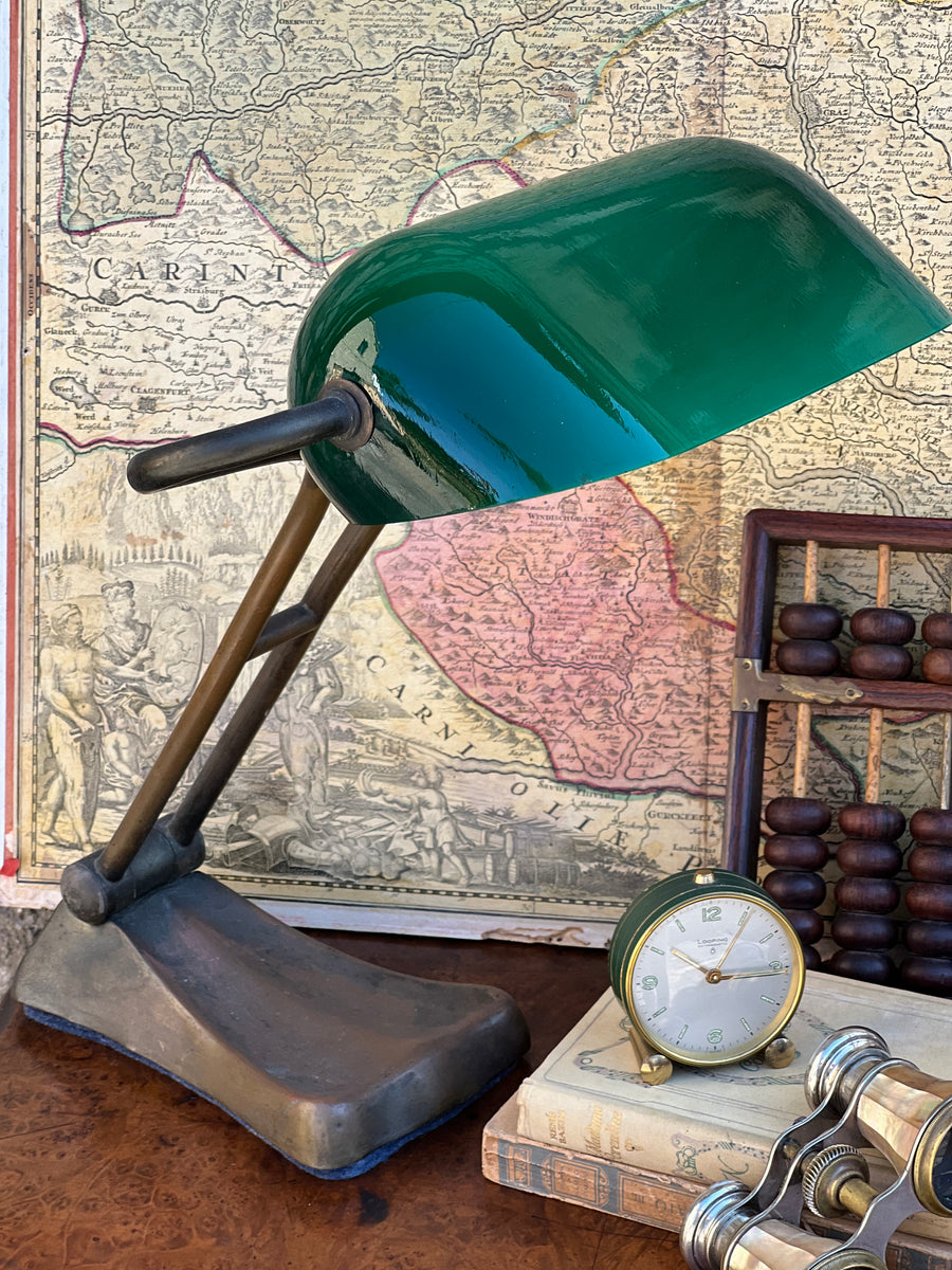 Lampada da tavolo in stile ministeriale con struttura in bronzo e paralume in vetro di colore verde. E' stat realizzata nella prima metà del Novecento e sia il paralume che la struttura sono regolabili. La forma sinuosa e la tonalità vibrante del vetro creano un'atmosfera calda e accogliente, perfetta per qualsiasi ambiente domestico o ufficio che richieda un tocco di stile retrò.&nbsp;

Misure base 19x12 cm; paralume 23x12 31x14x10 cm Altezza 43 cm