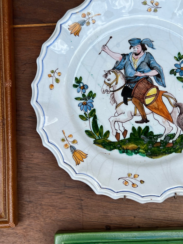 Piatto da parete in maiolica Nove di Bassano con raffigurato&nbsp;un uomo a cavallo alle prese un tamburo in abiti tradizionali. Il bordo del piatto è ondulato contornato da una linea blu.

I colori sono brillanti e ben conservati, grazie alla qualità della ceramica e della pittura.

Diametro 27 cm&nbsp;