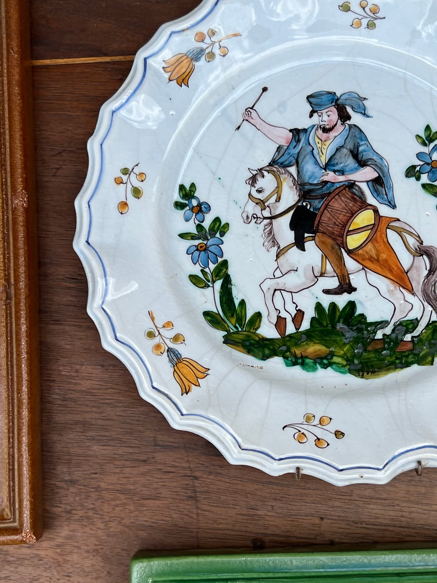 Piatto da parete in maiolica Nove di Bassano con raffigurato&nbsp;un uomo a cavallo alle prese un tamburo in abiti tradizionali. Il bordo del piatto è ondulato contornato da una linea blu.

I colori sono brillanti e ben conservati, grazie alla qualità della ceramica e della pittura.

Diametro 27 cm&nbsp;