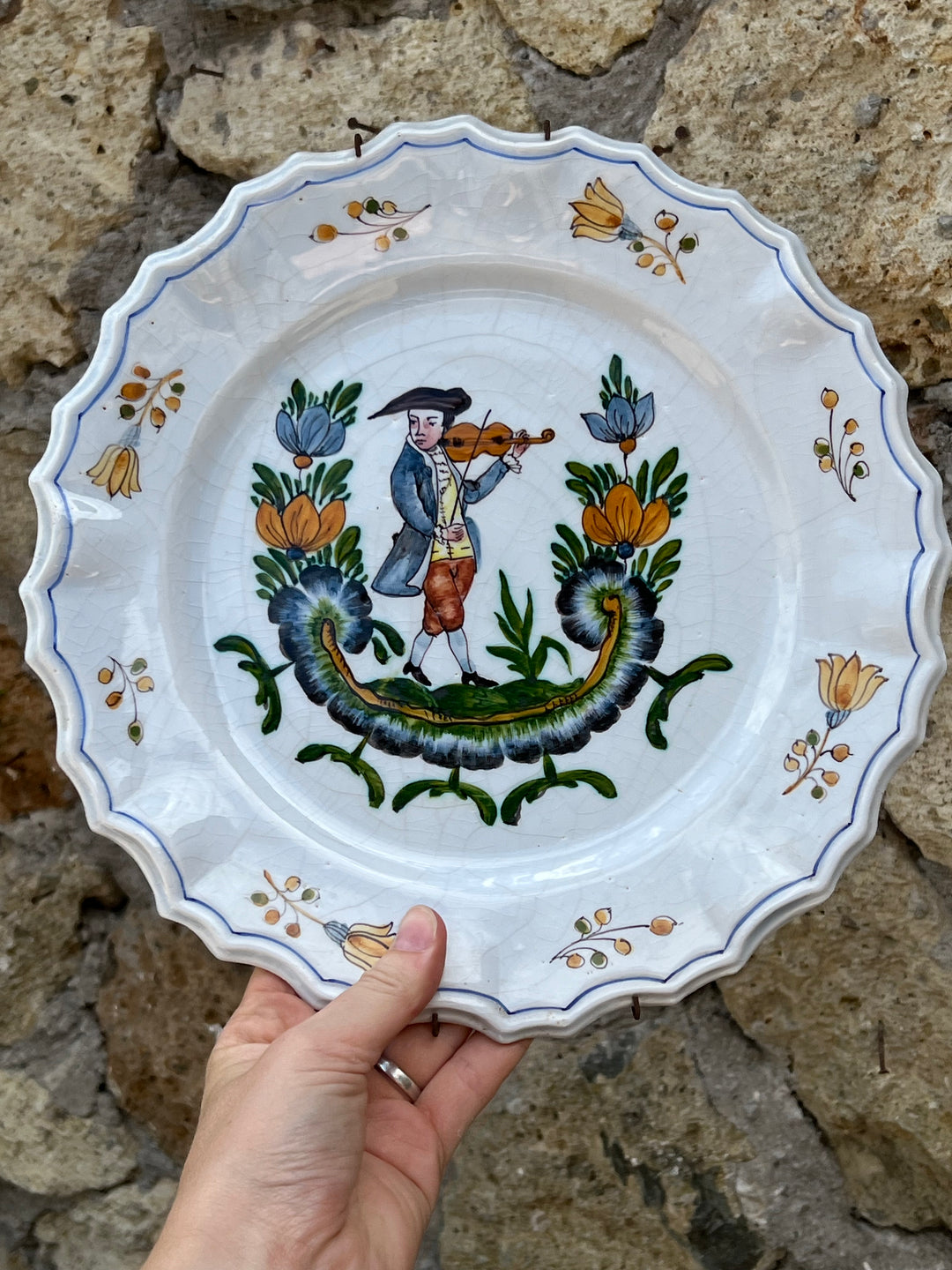 Piatto da parete in maiolica Nove di Bassano con raffigurato un uomo che suona un violino in abiti tradizionali. Il bordo del piatto è ondulato contornato da una linea blu.

I colori sono brillanti e ben conservati, grazie alla qualità della ceramica e della pittura.

Diametro 27 cm&nbsp;