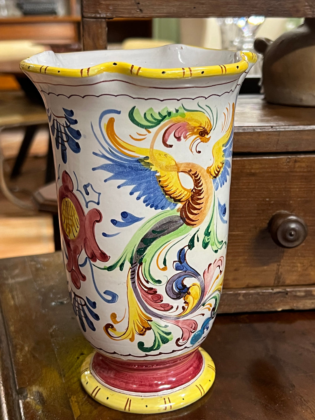 Vaso in ceramica italiana decorato a mano con vivaci motivi floreali e un meraviglioso uccello stilizzato in volo.

I colori accesi, come il giallo, il verde, il rosso e il blu, si combinano armoniosamente, donando un aspetto vivace al vaso. Il suo bordo ondulato e la sua forma sinuosa lo rendono un pezzo perfetto per arricchire l'arredamento di casa con un tocco di stile classico.&nbsp;

Misure 13x20 cm